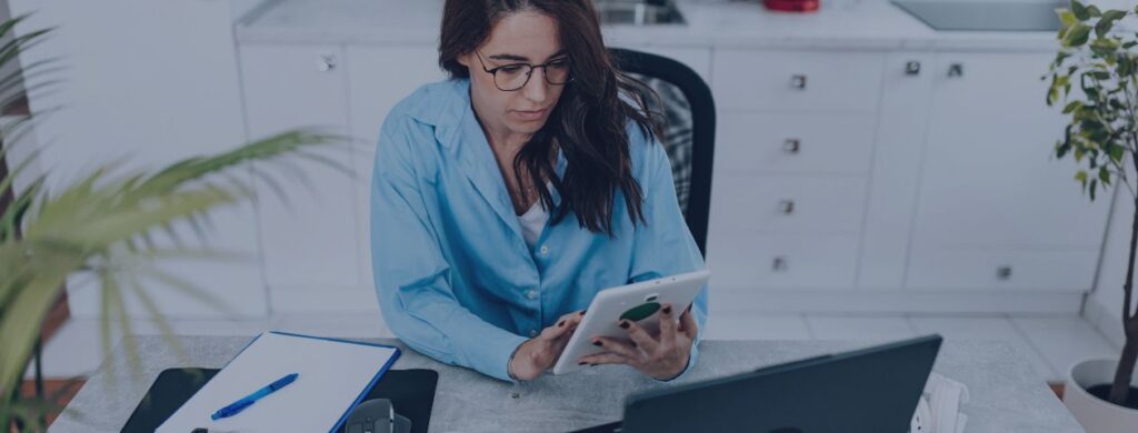 Wirtualna asystentka od social mediów - kobieta siedząca przy biurku, przed laptopem, trzymająca w ręku tablet, obsługująca social media - Aleksandra Łabaj